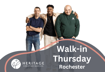 Three men standing together, smiling. Text reads: Walk-in Thursday in Rochester with Heritage Christian Services and the organization’s logo on a gray and orange wave design.